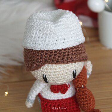 Gehäkelte Amigurumi-Kochpuppe mit weißer Mütze, roter Schürze und gehäkelten Würsten