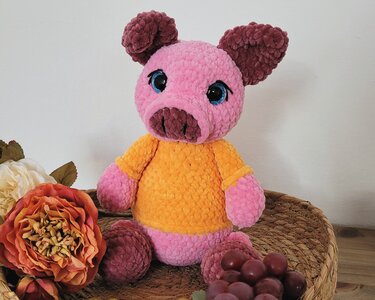 Gehäkeltes Amigurumi-Schweinchen in Rosa und Braun mit orangefarbenem Shirt und großen Augen in einem Weidenkorb