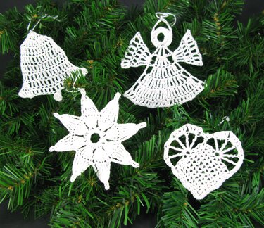 Vier schnell gehäkelte weiße Weihnachtsanhänger (Glocke, Engel, Stern, Herz) auf Tannengrün