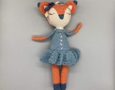 Gehäkelte Amigurumi-Fuchs-Puppe in hellblauem Kleid auf neutralem Hintergrund