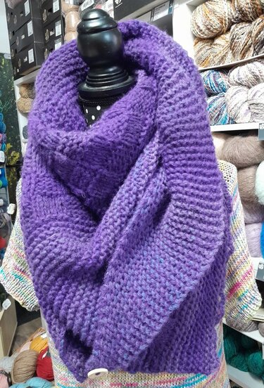 Schaufensterpuppe tr
gt volumin
sen violetten Grobstrick-Loop, Hintergrund Regale mit Garnen