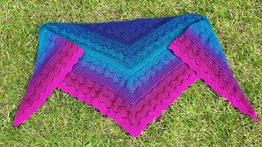 Gehäkeltes Dreieckstuch in Blau, Türkis, Lila und Pink mit Wellenmuster auf Gras.