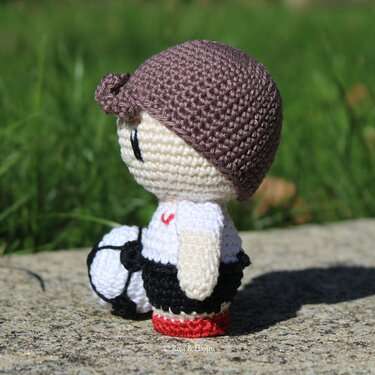 Seitenansicht eines gehäkelten Amigurumi-Jungen mit brauner Mütze und Fußball