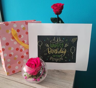 Geburtstagskarte mit dem Schriftzug "Happy Birthday to you" auf dunklem Feld, dekoriert mit Torte, Ballons, Rosen und gepunkteter Geschenktüte.