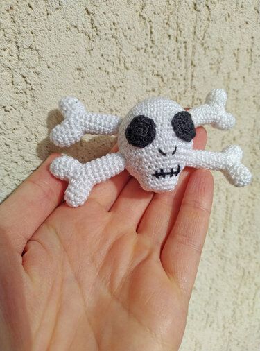 White crocheted skull and crossbones amigurumi with black eyes held in a hand.