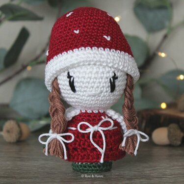 Gehäkelte Amigurumi-Puppe im Fliegenpilz-Design, rote Mütze mit weißen Punkten, rotes Kleid, geflochtene Zöpfe.