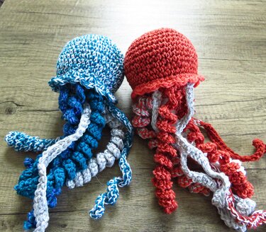 Zwei gehäkelte Amigurumi-Quallen auf Holz, eine blau-weiß, die andere rot-weiß