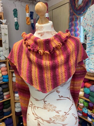 Gestricktes Dreieckstuch in Pink-, Orange- und Gelbtönen mit Streifenmuster und Rüschenkante auf einer Schneiderbüste.