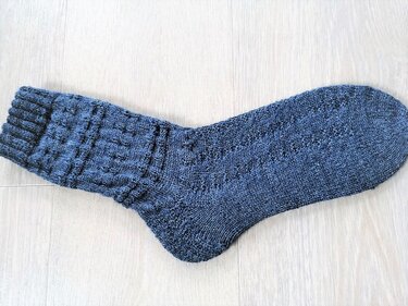 Dunkelgraue gestrickte Herrensocke mit Rippenbündchen und Strukturmuster auf hellem Holzuntergrund
