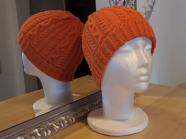Nahaufnahme einer orangefarbenen gestrickten Mütze mit Zopfmuster auf Styroporkopf