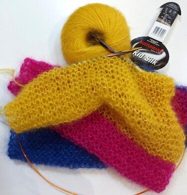 Gelbes flauschiges Garnknäuel, Rundstricknadel und mehrfarbiges gestricktes Stück in Gelb, Pink und Blau auf hellem Hintergrund.