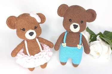 Two brown crocheted amigurumi teddy bears, one in a pink ruffled skirt with a bow and one in blue suspender pants