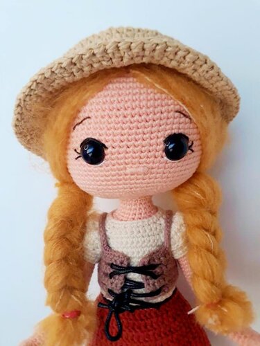 Handmade amigurumi doll with orange braided pigtails, beige crocheted hat, brown laced vest and red skirt