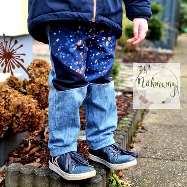 Beine eines Kindes in zweifarbiger Kinderhose mit Punktemuster oben und jeansähnlichem Stoff unten, blaue Sneaker