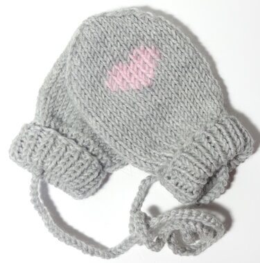 Gestrickte hellgraue Babyfäustlinge mit rosa Herz und verbindender Kordel auf weißem Hintergrund