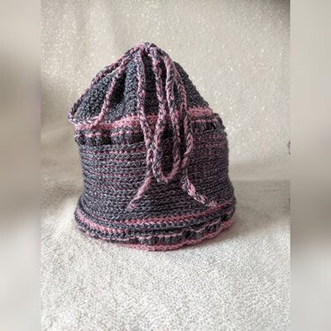 Handgehäkeltes Utensilo in Grau und Pink mit Kordelzug auf hellem Untergrund.