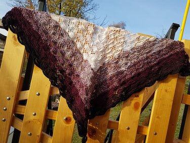 Gehäkeltes Dreieckstuch mit Farbverlauf von Burgund zu Creme, filigranes Spitzenmuster, auf Holzgeländer drapiert