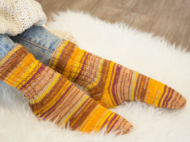 Gestrickte gestreifte Socken in Gelb, Braun und Violett auf weißem Teppich