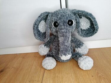 Grau-weißer gehäkelter Amigurumi-Elefant mit großen Ohren sitzt auf Holzboden