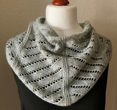 Hellgraues, gestricktes Dreieckstuch mit diagonalem Ajourmuster auf einer Büste.
