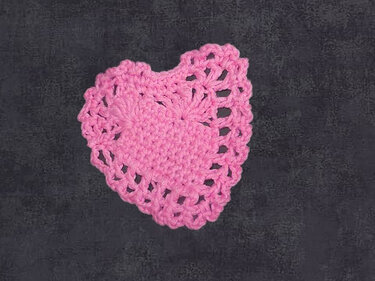 Gehäkeltes rosa Herz mit Spitzenrand auf dunklem Hintergrund