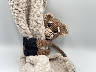 Hand-crocheted monkey holding a cream plush baby blanket