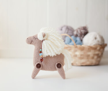 Beige crocheted amigurumi pony with white yarn mane and button legs