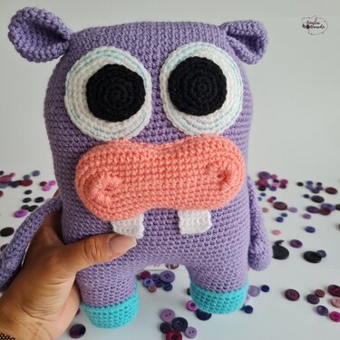 Lila gehäkeltes Amigurumi-Nilpferd mit rosa Schnauze und großen Augen, von einer Hand gehalten