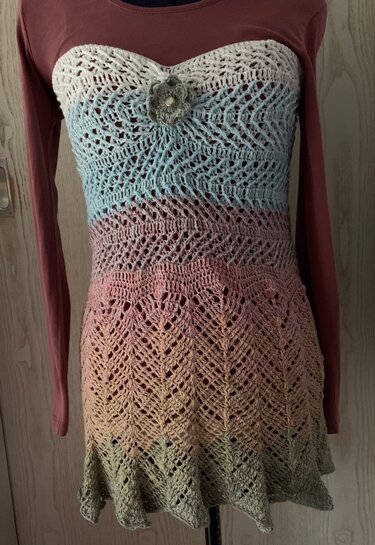 Gehäkeltes Bandeau-Top in Pastell-Farbverlauf mit Spitzendetails und Blumenapplikation auf einer Schaufensterpuppe.