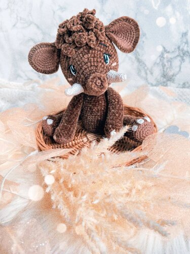 Braunes gehäkeltes Amigurumi-Wildschwein mit weißen Stoßzähnen im Körbchen, umgeben von Pampasgras