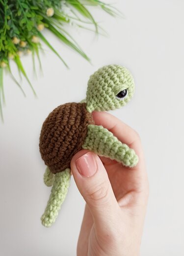Hand holding a small green and brown crochet turtle amigurumi with visible stitches.