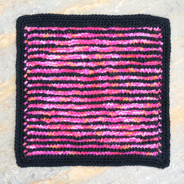 Quadratisches Strickstück mit pinken, orangen, gelben und schwarzen Streifen und schwarzem Rand