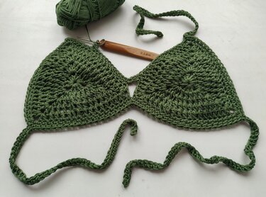 Green crochet triangle bikini top mid-project with 2.5 mm crochet hook and yarn ball