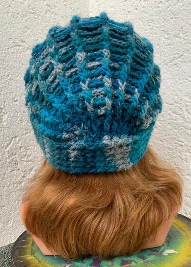 Rückansicht einer gehäkelten Damenmütze in Blau-Grün auf Schaufensterkopf