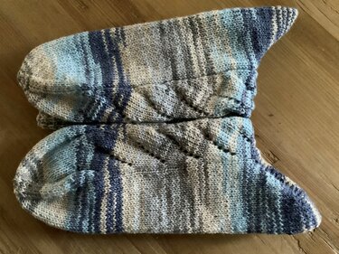 Ein Paar gestreifte, gestrickte Socken in Blau- und Grautönen auf einem Holzboden.
