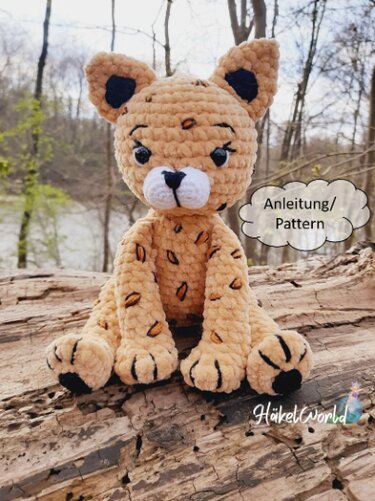 Gehäkeltes geflecktes Amigurumi-Katzenbaby aus samtigem Garn, sitzend auf einem Baumstamm