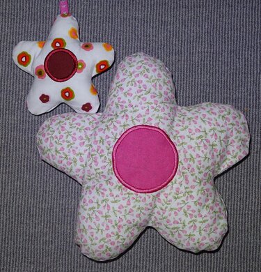 Gefüllte gestickte Stoffblume in Rosa‑Grün und bunter Sternanhänger auf grauem Untergrund.