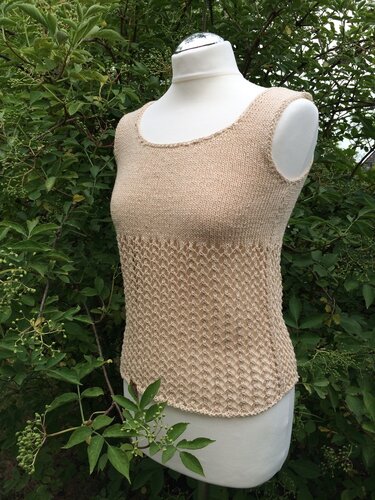 Beigefarbenes ärmelloses Stricktop mit Lochmuster auf einer Schneiderpuppe vor grünen Blättern.