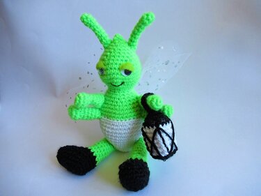Gehäkeltes grünes Amigurumi-Wesen mit Fühlern, glitzernden Flügeln und kleiner Laterne