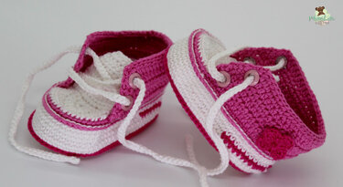 Zwei gehäkelte Babyschuhe in Pink und Weiß im Sneaker-Design mit Schnürsenkeln