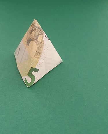 Gefaltete Pyramide aus einem 5‑Euro‑Schein auf grünem Untergrund