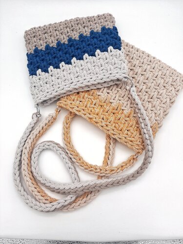 Rechteckige gehäkelte Umhängetasche mit blau-grauem Zickzackmuster und geflochtenem Trageriemen; gold-beige Tasche im Hintergrund.