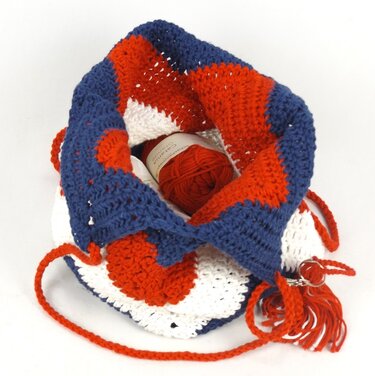 Gehäkelte Umhängetasche rot‑weiß‑blau mit Kordelzug und Garnknäuel