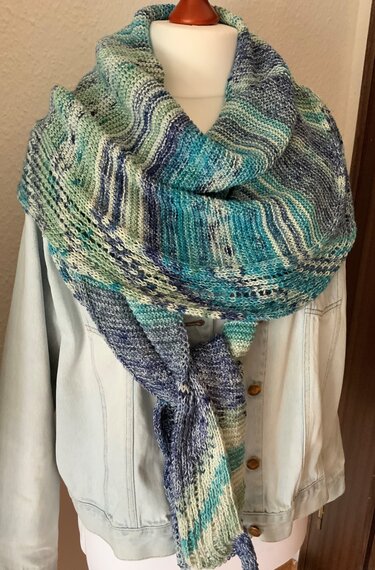 Gestricktes Dreieckstuch in Blau, Türkis und Grün mit Lochmuster, drapiert über eine helle Jeansjacke an einer Schaufensterpuppe