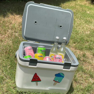 Geöffnete Kühltasche mit Dosen und Flaschen; vorne zwei bunte Aufkleber: Wassermelone und Eis am Stiel