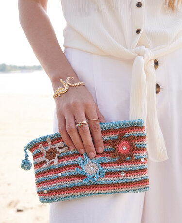 Gehäkelte Clutch mit Pastellstreifen, Blumenapplikationen und kleinen Glitzersteinchen, gehalten von einer Hand