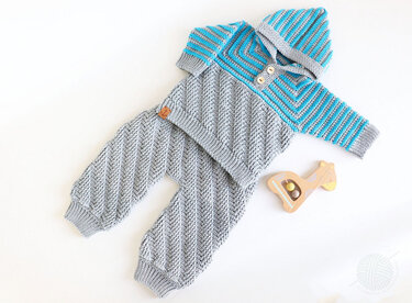Grey and blue crocheted baby outfit with a hooded top, wooden buttons and chevron pants beside a wooden toy.