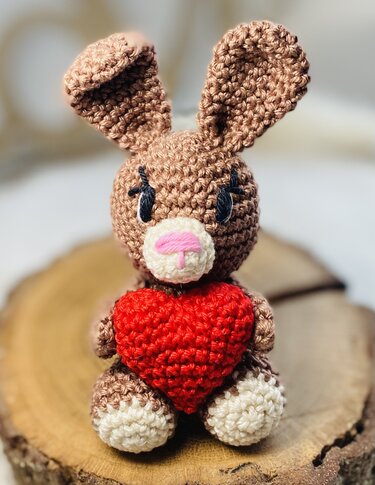 Gehäkelter brauner Amigurumi-Hase mit rotem Herz auf Holzscheibe