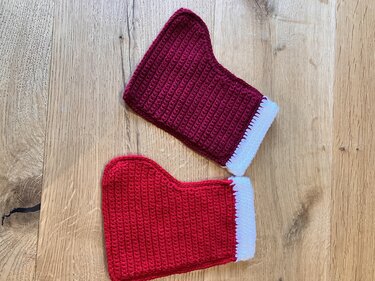 Zwei gehäkelte Nikolausstiefel in Rot und Dunkelrot mit weißem Saum auf einer Holzoberfläche