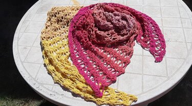 Zwei gehäkelte Dreieckstücher in Gelb und Pink auf rundem Tisch